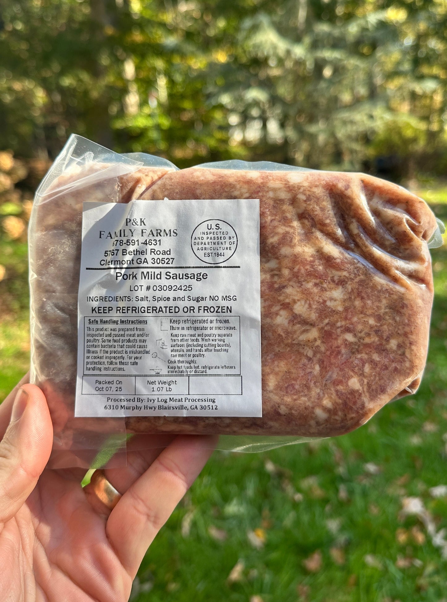 Packaged pork mild sausage held in a hand with a natural background