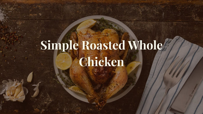 Roasted chicken on a plate with lemons and herbs with overlay text, Simple Roasted Whole Chicken