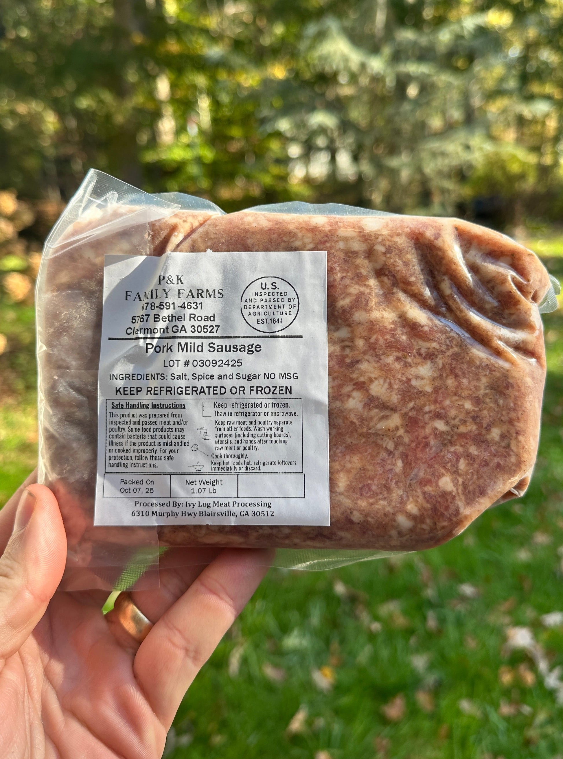 Packaged pork mild sausage held in a hand with a natural background